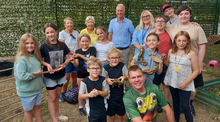 "Group of Action for Family Carers young carers and staff smiling and holding animals, including snakes and lizards, during a petting zoo activity at a club session."