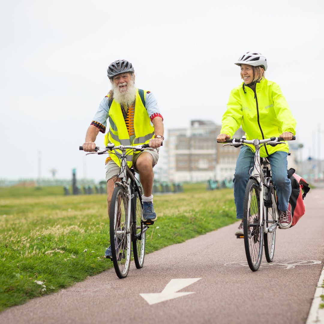 a man and a woman cycling in high vis jackets smiling.