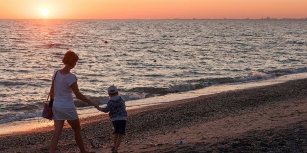 Carer walking with a child on a beach at sunset, symbolising family caring and support.