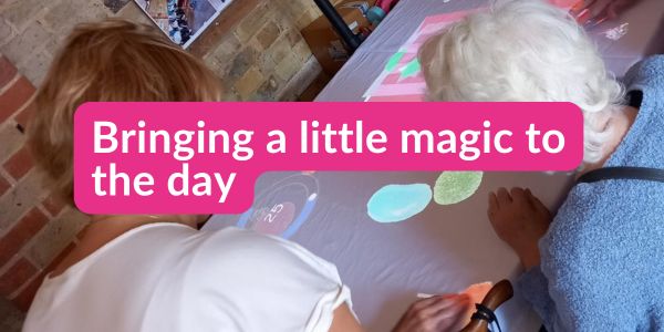 Two people taking part in a creative activity together, touching colourful shapes on a table at a day centre